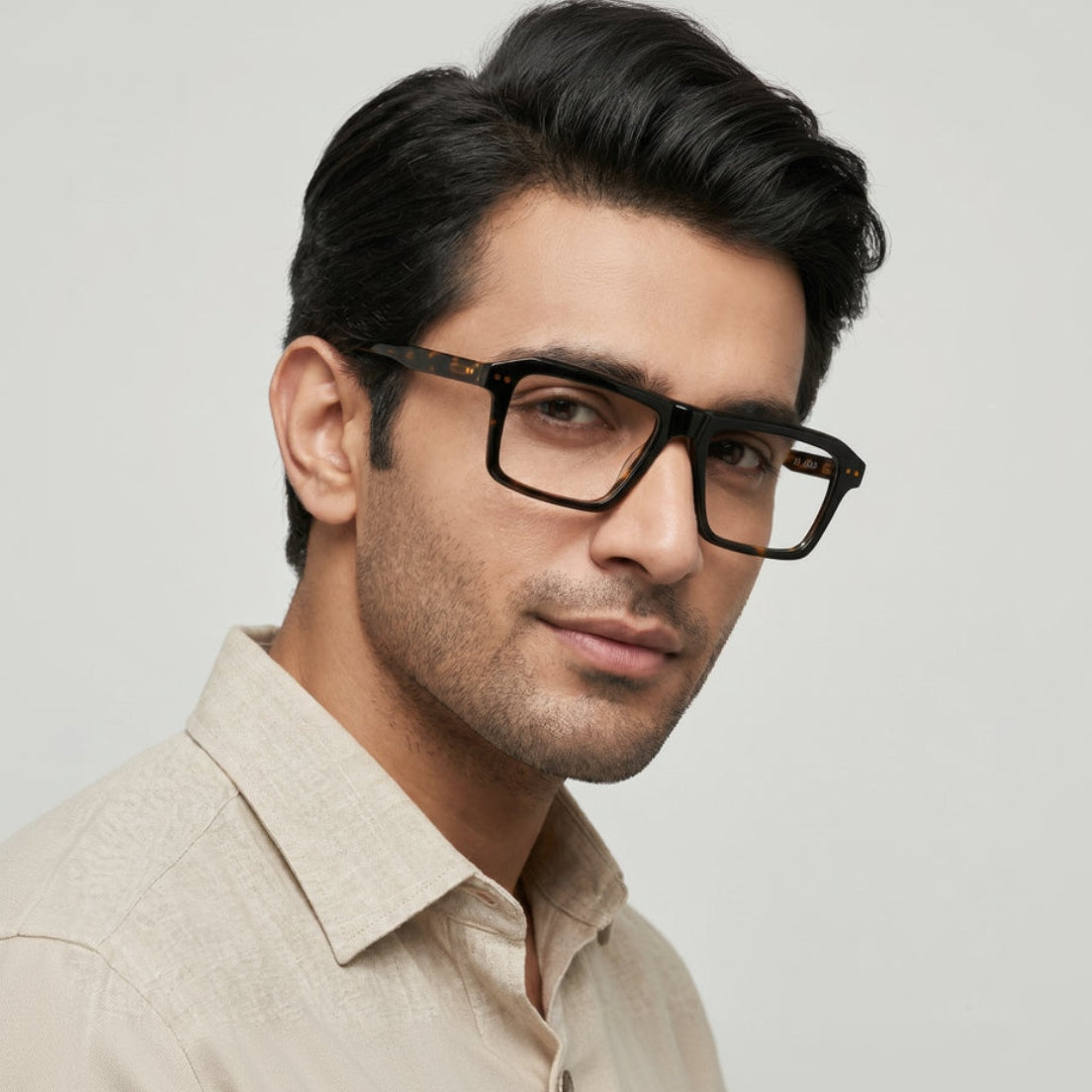 Man wearing black glasses and a beige shirt against a light gray background